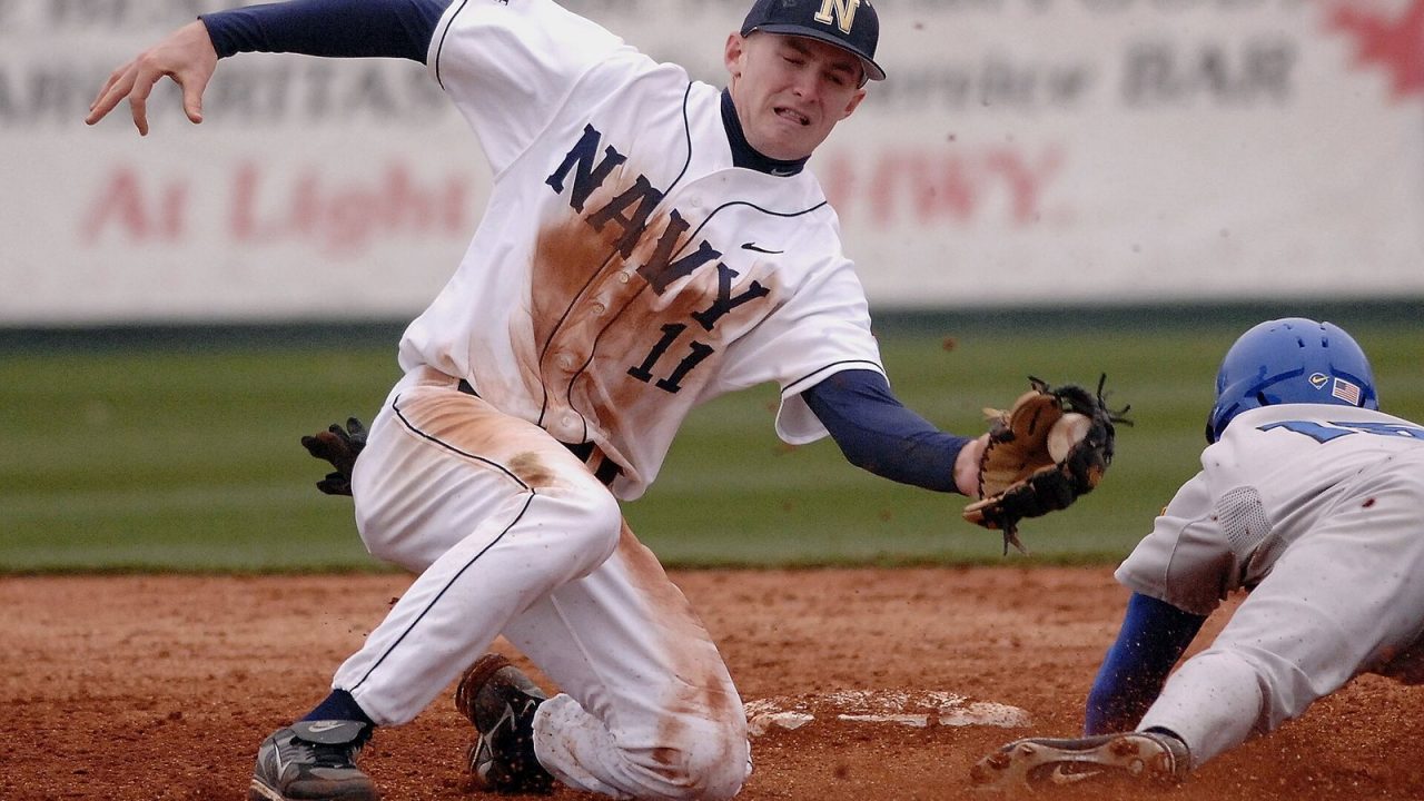 Navy shortstop stretching to catch a throw from his catcher at second base during a college game